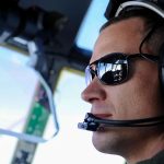 A pilot wearing sunglasses looking outside a plane's window