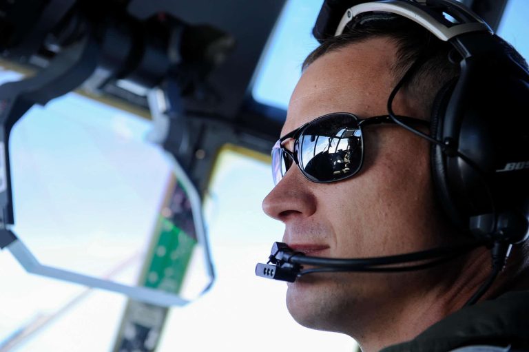 A pilot wearing sunglasses looking outside a plane's window