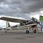 A man on top of a white and purple Cessna 180 plane on the runway