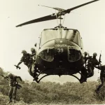 A Huey helicopter with soliders jumping out of it