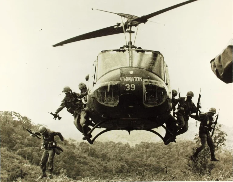 A Huey helicopter with soliders jumping out of it