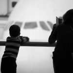 A mother and her son looking at a plane at the airport's gate