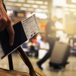 A man holding his boarding pass, passport and carry-on bag at the airport
