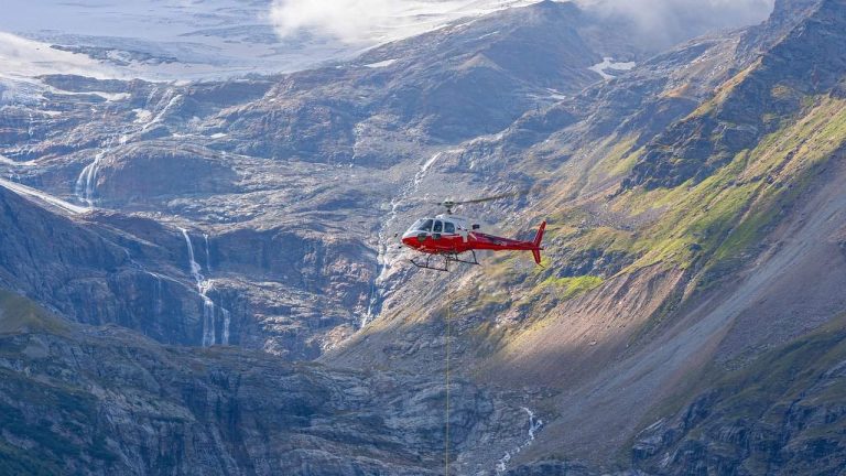 A red and white helicopter flying in a mountainous region