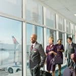 Two male flight attendants smiling with 3 female flight attendants