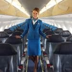 A flight attendant in blue uniform on a plane who is smiling