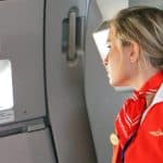 A flight attendant dressed in red looking outside a plane's window