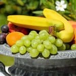 A bowl of fruit containing bananas, grapes and apricots