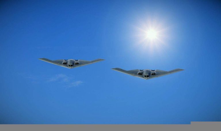Two American stealh bombers flying side by side in blue skies