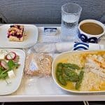 Airplane food meal containing chicken, a salad, bread, and a pastry
