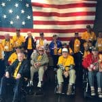 Honor Flights: What They Are and How They Honor Veterans A group of honor flight veterans with the US flag sitting and standing in front of the US flag