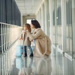 Child standing with her suitcase and her mom at an airport