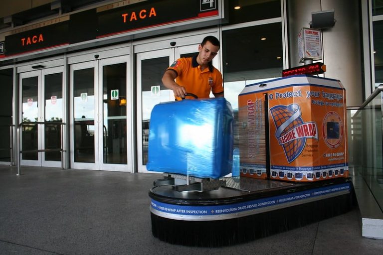 a man wrapping a blue suitcase in plastic